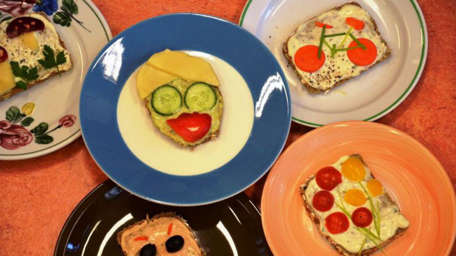Kreativ belegte Brot für Kinder mit Gesichtern, Fahrrad und Blumenwiese aus Gemüsestücken.