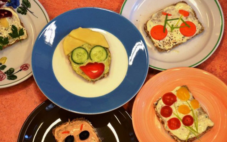 Kreativ belegte Brot für Kinder mit Gesichtern, Fahrrad und Blumenwiese aus Gemüsestücken.