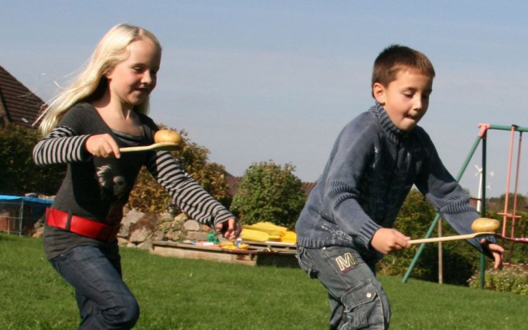 zwei Kinder balancieren einen Erdapfel auf einem Kochlöffel